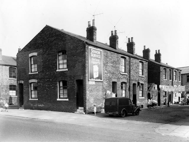 Clothes are visible hung on lines stretched across the street while prams stand facing house entrances on Eastwood Street in September 1959. On the left of the image are two houses located in the gable end of the terrace, numbers 44 and 46 Cross Stamford Street.
