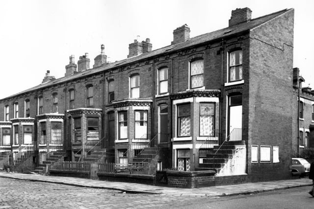 Ascot Place in October 1966. Back-to-back terraced houses with large bay windows and steps leading up to a first floor entrance. In front, each house has a small private garden. On the end wall are advertisements including one for the Burmantofts Regent Picture House. Visible on the right are houses on Ascot Street.
