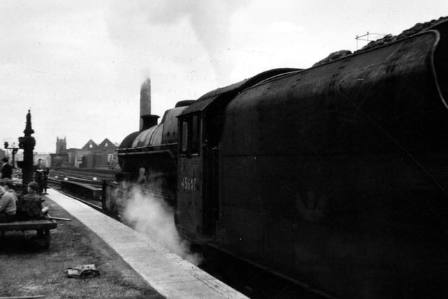 A 'Jubilee' class steam locomotive number 45647, named 'Sturdee', waits to leave Leeds City station. A holidaymakers' express to the West Coast, this train would run every Saturday only for a couple of months. The backing-plate for the locomotive's nameplate is visible just above the escaping steam - the nameplate itself is missing - either removed or sometimes they had been stolen.