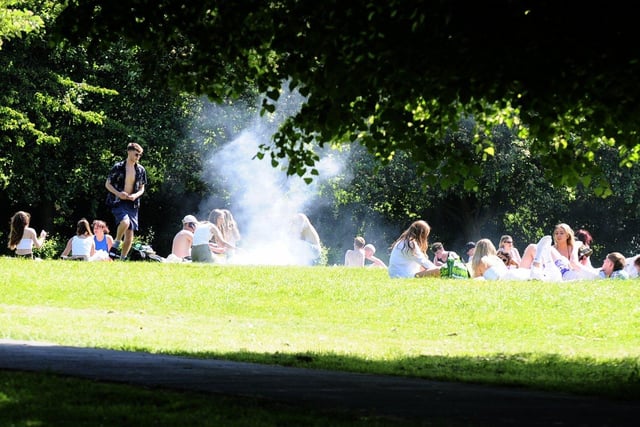 Locals taking in the sun at Woodhouse Moor as smoke bellows out.
