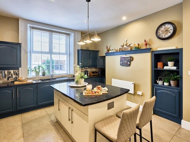 The kitchen features navy cabinetry that conceals integrated appliances and a double wall-mounted oven, a central island and bespoke cupboards and shelving that have been created to fill the original alcoves.