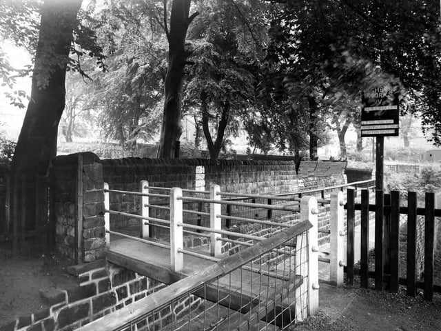 The bridge over Meanwood Beck pictured in June 1948. The concrete footbridge crosses the beck as it flows through a stone channel between Highbury Cricket Club's pitch on the right, and Meanwood Park on the left (over the stone wall). A sign advertising a match between Highbury Works C.C. and Calverley is visible.