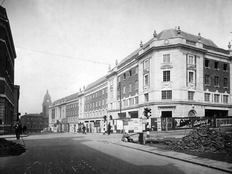 Block of buildings ran from Albion Street to Cookridge Street. Built to design of Sir Reginald Blomfield and G.W Atkinson by the Leeds Corporation cost £120,000. Nine shops at ground level, four floors of offices above, large number leased to Inland Revenue. Leeds Town Hall can be seen to left. Hoardings round building carry posters. Some for products 'Oxo', Bovril, Andrews Liver salts, most for local events. A man is looking into site on right. Traffic lights at road junction. Pictured in July 1931.