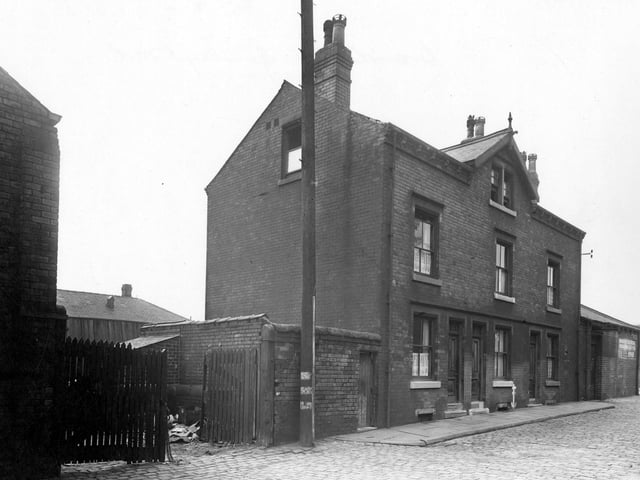 The gates of the yard at Thomas West Ltd, Cooper, of Brandon Street. There is a high wall and wooden gates at the entrance. On the right is a terrace of three houses. Pictured in September 1950.