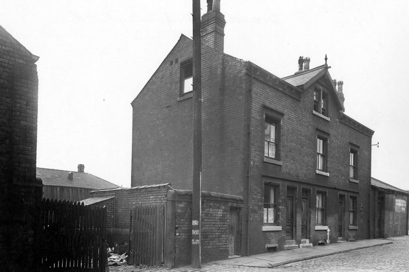 The gates of the yard at Thomas West Ltd, Cooper, of Brandon Street. There is a high wall and wooden gates at the entrance. On the right is a terrace of three houses. Pictured in September 1950.