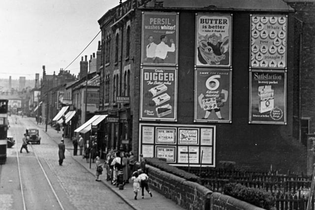 A view looking from Barrack Street along Meanwood Road in June 1955. H Rayman, financier at 54 Meanwood Road is on the right. Advertising posters can be seen on cable end of building.
