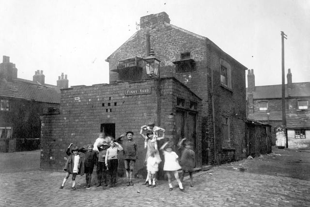 A group of children pose for the camera on Finny Yard, a plot of land between Low Road and Church Street. The brick building in the centre has a pigeon loft a block of outside toilets in front of it.