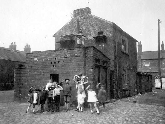 A group of children pose for the camera on Finny Yard, a plot of land between Low Road and Church Street. The brick building in the centre has a pigeon loft a block of outside toilets in front of it.