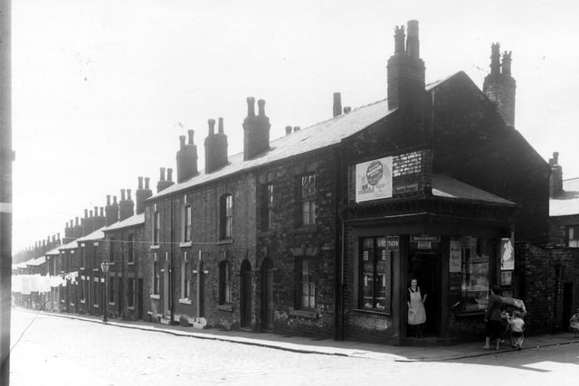 Grange Street runs from the left edge of this view in ascending order to number 81 on the right. Number 81 is part of the shop premises seen on the right at number 20 Green Lane which is listed as the business of Mrs Maggie Butler. A lady in an apron stands in the doorway while a woman pushing a pram with a little boy look into the window. Pictured in June 1959.