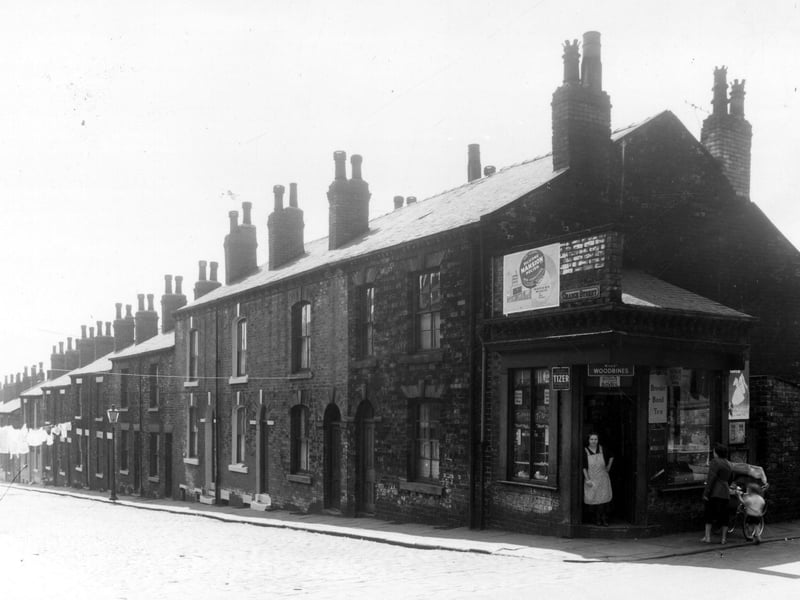 Grange Street runs from the left edge of this view in ascending order to number 81 on the right. Number 81 is part of the shop premises seen on the right at number 20 Green Lane which is listed as the business of Mrs Maggie Butler. A lady in an apron stands in the doorway while a woman pushing a pram with a little boy look into the window. Pictured in June 1959.