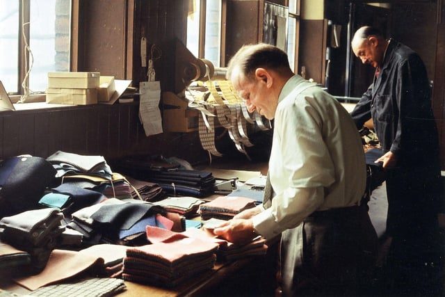 Manager Henry Atkinson and head dyer Bob Goodall examining a selection of pattern books, used to send to potential customers, in the weaving office of J.& S. Rhodes Ltd in July 1965. The firm owned three mills in Morley - the Prospect, the Queens and the Valley. The Valley Mills was first to close in the 1950s. Queens Mill, where Henry Atkinson had been manager, closed about 1960. It was situated immediately behind Morley Town Hall and was affected by the disastrous fire in August 1961 at its neighbouring mill, Albert Mills, when the dome of the Town Hall was also damaged. Because of this the Queens Mill and Albert Mills were demolished by the middle of 1962. Mr. Atkinson transferred once more to Prospect Mills.
