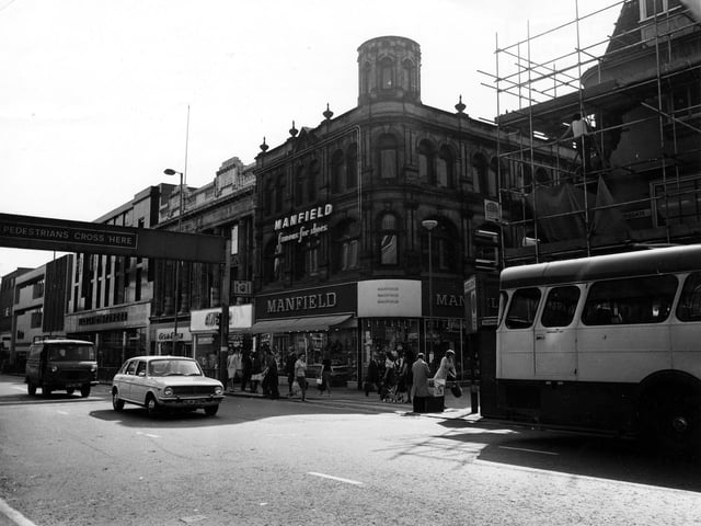 The west side of Briggate showing the junction with Commercial Street in June 1975. In the centre is Manfield footwear, to the left of this is Amber ladieswear, Trueform footwear and Marks and Spencer. On the right of the picture, hidden behind a bus and scaffolding, is H.Samuel, jewellers. A car and van are also on the road.