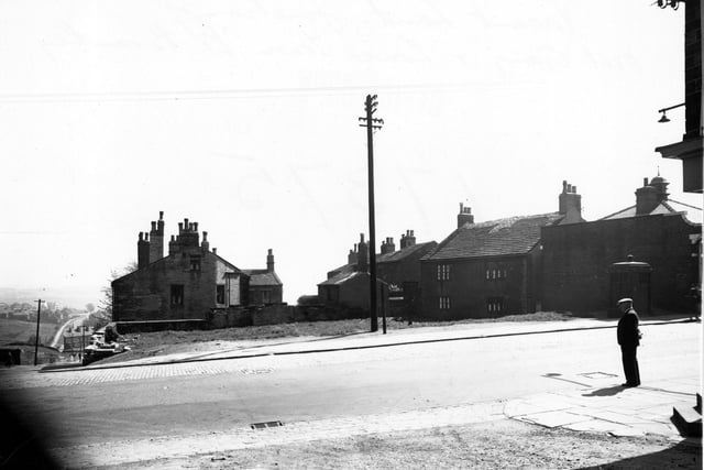 Vacant land on Lower Town Street by the junction with Out Gang Lane in May 1950. A police phone box, an old man, a telephone pole and a drain grate are visible.