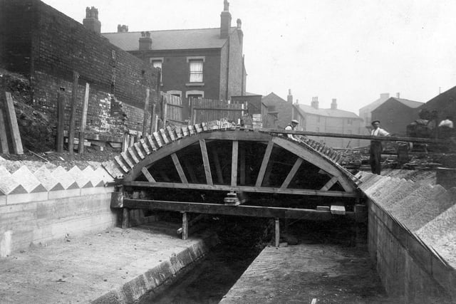 Construction of a beck covering over Sheepscar Beck at Whitelock Street. The beck runs in a stone channel under a timber "form", over which the brick covering is being built. There are workmen and a concrete mixer in the picture, and terraced houses and other buildings in the background. The block of terrace houses to the right is Valley Street. Pictured in June 1928.