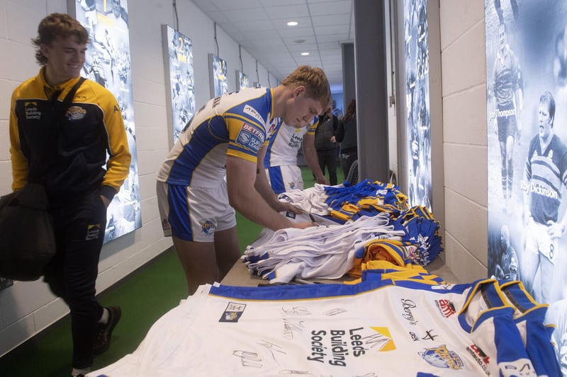 Forward James McDonnell signs shirts at Leeds Rhinos' photocall and media day as 17-year-old prospect Fergus McCormack looks on.