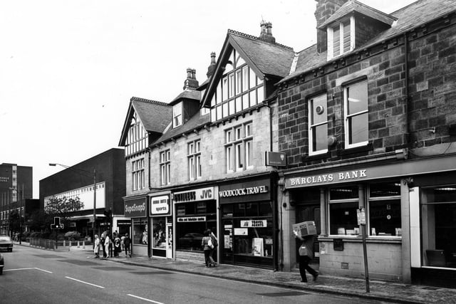 A man carrying a large box, possibly a TV, down Otley Road in March 1980. Shops and businesses include Barclays Bank, then Woodcock Travel Agents, Bradleys Video and TV Centre, Norman Hunter sports and SupaSnaps Film Processing. The Arndale Centre can be seen on the left, past the Wood Lane junction, with Arndale House towering in the background.