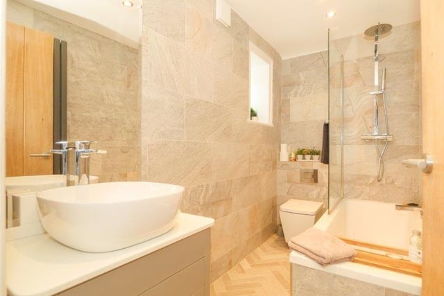 The bathroom features a luxurious three piece suite and includes an overhead mains powered rainfall shower, vanity style sink unit, wall mounted mirror and fully tiled walls and flooring.