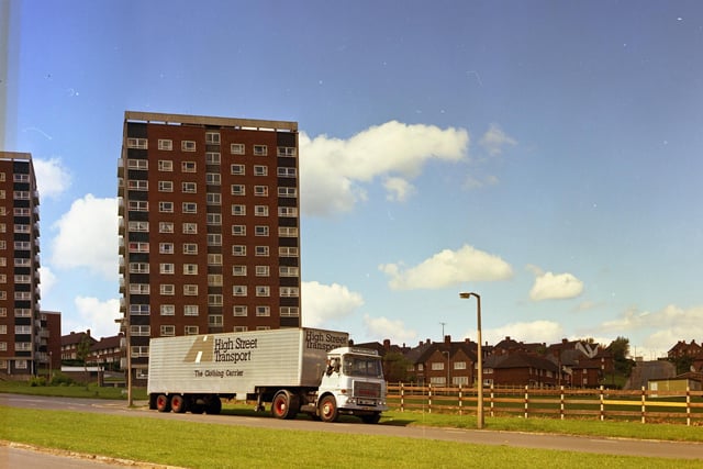 A High Street Transport lorry makes its way through Burmantofts  in June 1973. The driver leans out of the window. There are 1930s council houses in the background. A tower block is visible to the left of the lorry as well as low-rise council housing. This a Burton's company photograph.