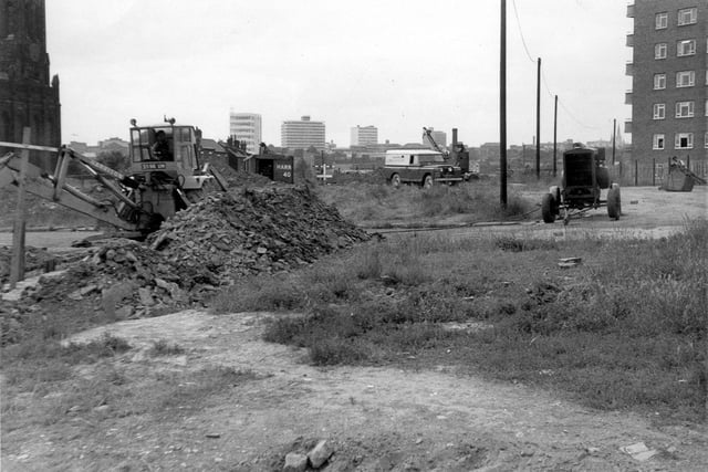 A view from land in the process of being cleared, the former site of old red brick terraced streets in  Mabgate. These included Lyndhurst Street, Old Hall Street and Gibson Street. Later Agnes Stewart C. of E. High School was built on the site. Across the centre of the image is St. Mary's Lane and part of St. Mary's Church can be seen at the left edge. At the right edge Cromwell Heights, high rise flats, are visible. Between the church and the flats New Church Place was once situated.