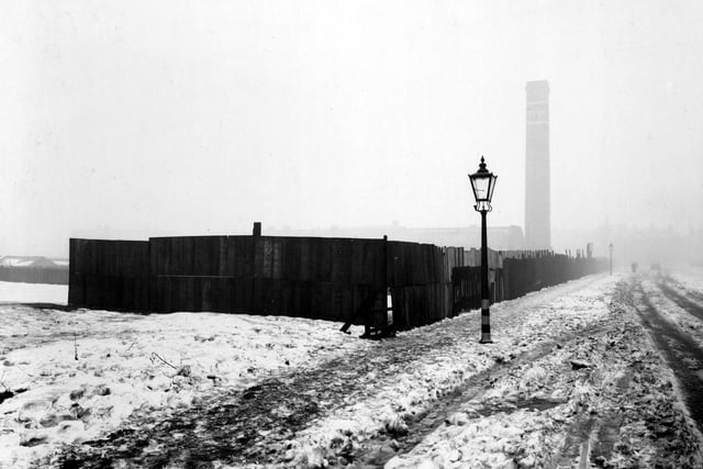 Barkly Road in February 1940. Fenced off area and gas lamp with black-out markings to base. Snow on the ground with tyre tracks on road and footprints on pavement. Large chimney dated 1848 in the distance.