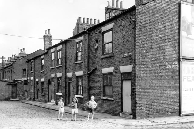 Back-to-back terraced houses from the junction of Mount Place on the left and Selkirk Street on the right in August 1964.  Three boys in short trousers, one holding a stick stand at the entrance to Mount Place while in the distance are the one storey yards originally built to house the shared outside toilet. On the far right it is possible to see a section of two advertising hoardings, one promoting eggs and the other the Hunslet Feast.