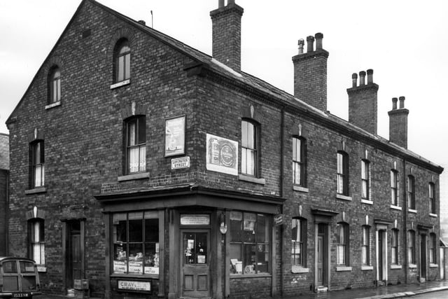 On the left is Lovington Street, while on the right is Benson Street. Number 42 is on the corner, a grocers and off licence, licensed to Mr Charles Albert Clapham. Products advertised for sale include Steradent denture cleaner, Cardinal polish, Brooke Bond tea and a variety of cigarettes. Numbers 36 to 40 on the right are back-to-back terraced houses with a row of shared outside toilets accessed on the right. Pictured in April 1967.