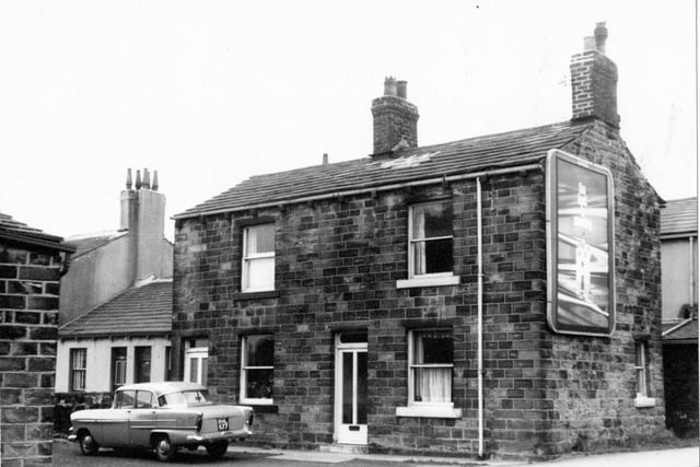 Two stone terraced houses on Whitehall Road with one over one sash windows. In front of terrace is a 1960s car number plate RHL 677 and on gable end of terrace on right is an advertising hoarding. Visible on the far left are the one storey white cottages of nos. 271-283 Whitehall Road. Pictured in March 1967.