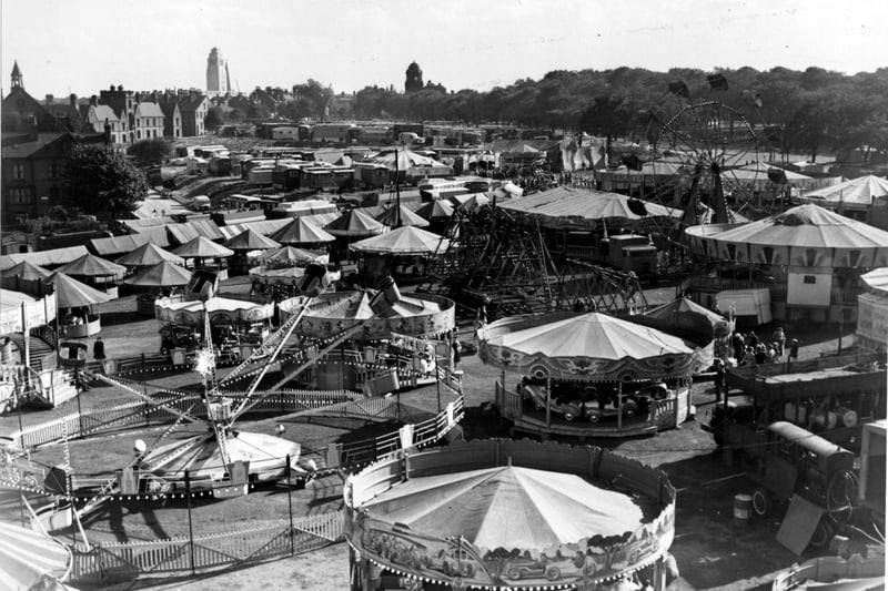 Woodhouse Feast fair on Woodhouse Moor in September 1955. People can be seen on or near various rides and stalls. Crossfield Street, Leeds University and the Woodhouse Library can be seen in the background.