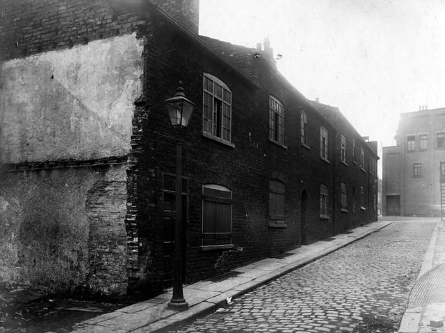 A view of properties in Back Virginia Street looking from the direction of Prussia Street to Virginia Cross Street. Back Virginia Street is situated between Virginia Street and Nelson Street. These partially demolished brick houses are on two storeys with old, multi-paned windows. There were several arched entrances to passageways accessing Nelson Street but only two remain in this image. The building seen at the end is in front of the Black Swan public house which is located at number 90 Vicar Lane. Pictured in July 1928.