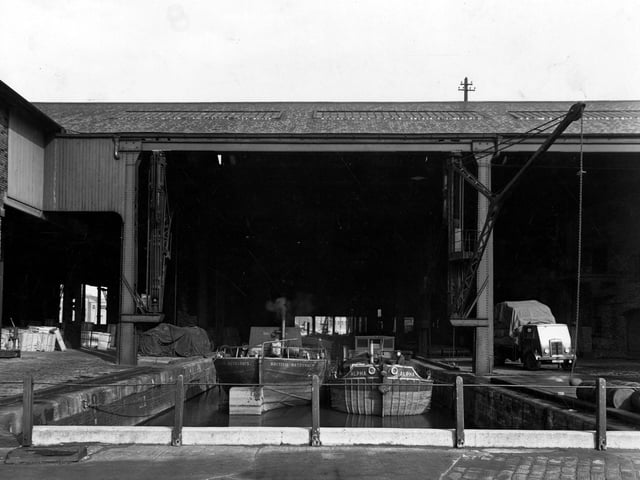 A view of British Waterways basin at Dock Street showing barges tied up to wet dock under a large building. On the dockside is a loaded lorry, barrels and packing cases. There is a crane with a chain on each side of the dock. Pictured in September 1950.