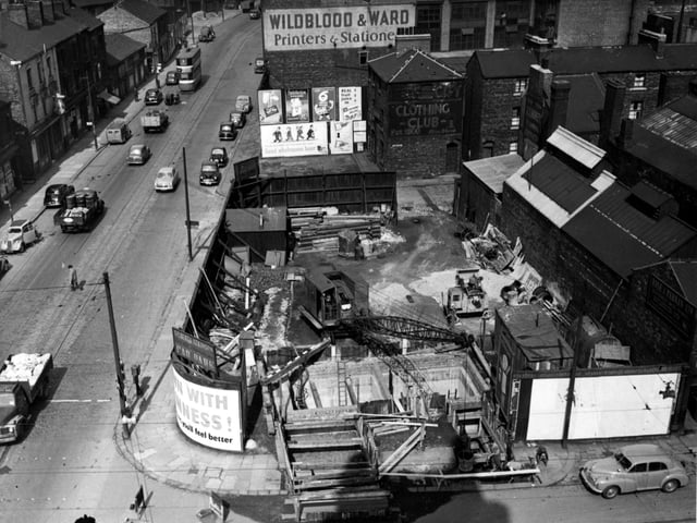 An aerial view of construction work on a sewer at the corner of Meadow Lane and Great Wilson Street in April 1955. A crane has its arm over the pit. Advertisements for Cadbury's Chocolate, Guinness, Chivers Jellies and others are visible. A painted sign for Wildblood & Ward, printers and stationers, can be seen.