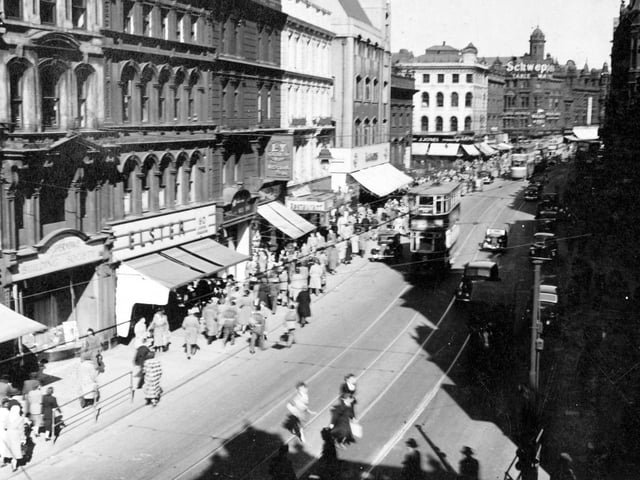 A sunny day looking east along Boar Lane from Albion Street in April 1951. It shows a busy street with people walking along the pavement. On the road are several trams and cars. Many of the shops have awnings and shop front advertising. You can see Elsters and J. Jones, L.V. Staidner, Westminster Bank and the Co-operative Building Society