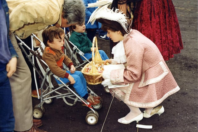 A young woman dressed in 18th century costume offers a basket of sweets to the little ones among the crowd that has assembled to watch the Lord Mayor's Parade set off from Woodhouse Moor.