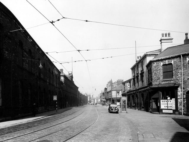 A view looking along Hunslet Road from the junction with Dawbridge Street in August 1947. W. Murrell hairdressers, The Royal George Hotel and Walton's fish and chip shop visible. Kingston and Co. engineering works on the left. Telephone box is prominent. Cars, pedestrians, tramlines and a tram stop can be seen.