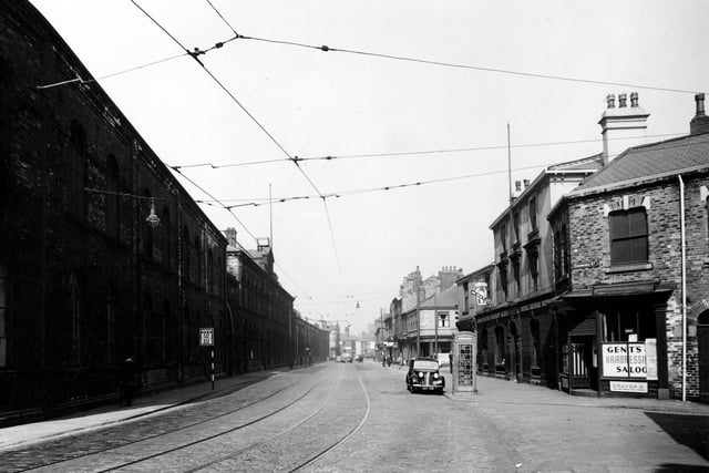 A view looking along Hunslet Road from the junction with Dawbridge Street in August 1947. W. Murrell hairdressers, The Royal George Hotel and Walton's fish and chip shop visible. Kingston and Co. engineering works on the left. Telephone box is prominent. Cars, pedestrians, tramlines and a tram stop can be seen.