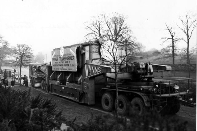 A 140 Ton load passing through Leeds in January 1956. People are stood around on the bottom left hand corner watching the load pass. A sign on the side of the trailer says "power transformer" made by the British Thompson-Houston Co. Ltd.