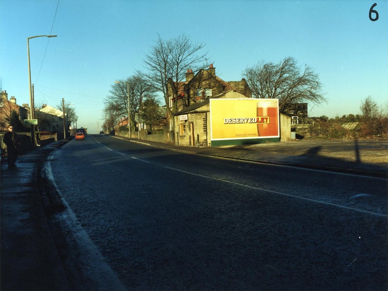 Bradford Road in Drighlington in December 1990. A fish and chip shop in the centre, with a large advertisement for Tetley's Bitter on the side. Further along the road is the Tempest Constitutional Club, and on the left hand side, the white building is the Painter's Arms public house.
