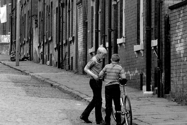 Two young boys are having a conversation, one of them with a bike.