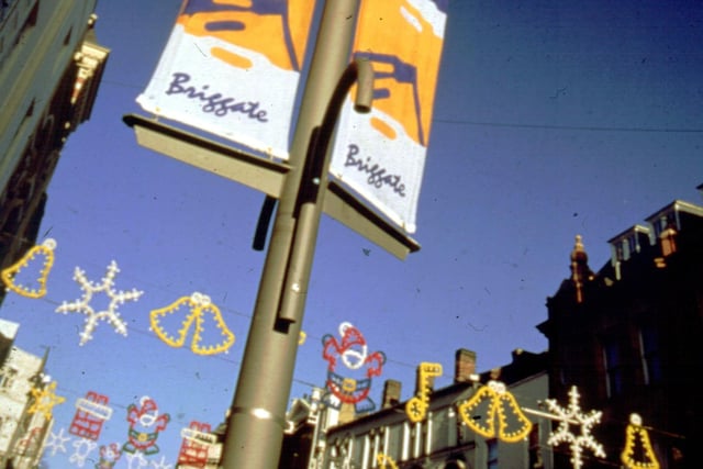 Christmas Lights strung across Briggate in 1999. A sign for Briggate advertises 'Leeds Shops'. The Christmas Lights are the work of the Leeds Lights Workshop which was formed by Leeds City Council in 1983.