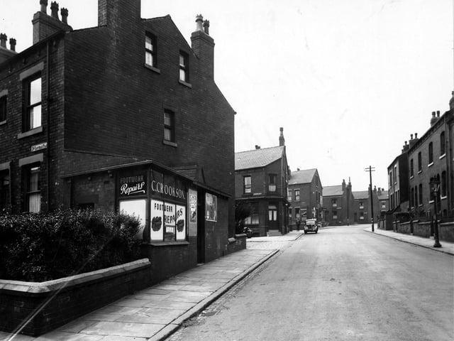 Looking west along Rowland Road in August 1949. C. Crookson footwear repairs are in the foreground. The ends of Clovelly Place and Clovelly Avenue are visible. A car, a man, streetlamp and telegraph pole can be seen.