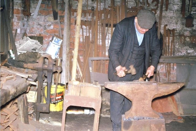 February 1971 and pictured is an inside view of the smithy belonging to George Shelton. He can be seen at work, fashioning metal on his anvils.