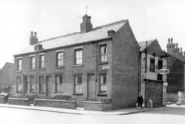 Roxburgh Street on the left, three blind back terraces each with a small private garden at the front surrounded by a wall. On the far right is Moorview Road with a woman carrying shopping bags followed by two children walking towards Roxburgh Street. On the right is the Moorview Garage, automobile and electrical engineers selling Esso and Cleveland petrol.  Pictured in August 1964.
