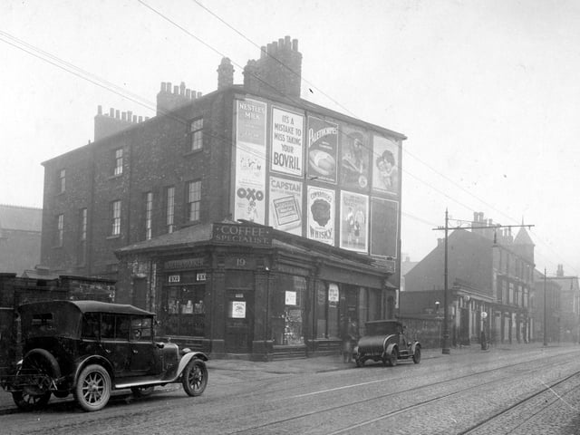 Roundhay Road which was the grocers shop premises of Walter Barker, with William Heaton, Boot and Shoe repairers at number 21. Advertising hoarding can be seen on gable end. Numbers 23, 25 and 27 is W. Mitchell Motors Ltd. Tramlines and overhead wires can be seen. Pictured in February 1930.