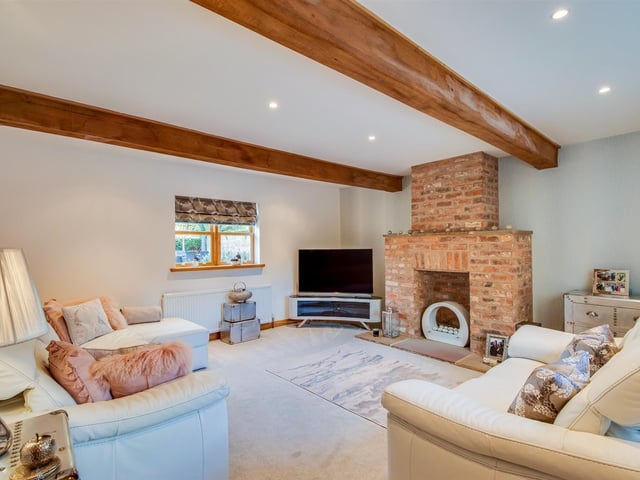 Wooden ceiling beams and a brick feature fireplace with chimney breast bring a rustic element to this comfortable sitting room.