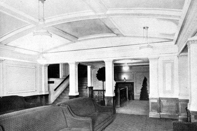 Inside the Majestic Cinema. There are upholstered sofas in the carpeted room and beyond the white pillars there is a staircase.