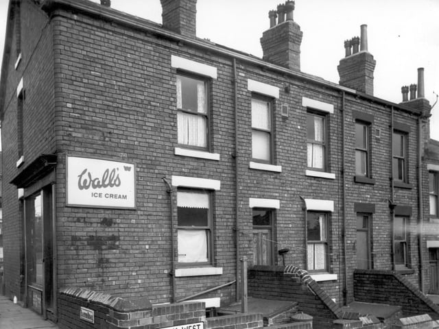The shop on the left is number 22 Barton Road, 'The Handy Shop'. An advertisement for Wall's Ice Cream occupies wall space on Back West View. The backs of terraced houses can be seen right of centre. There are steps up to the brick built outside toilets.