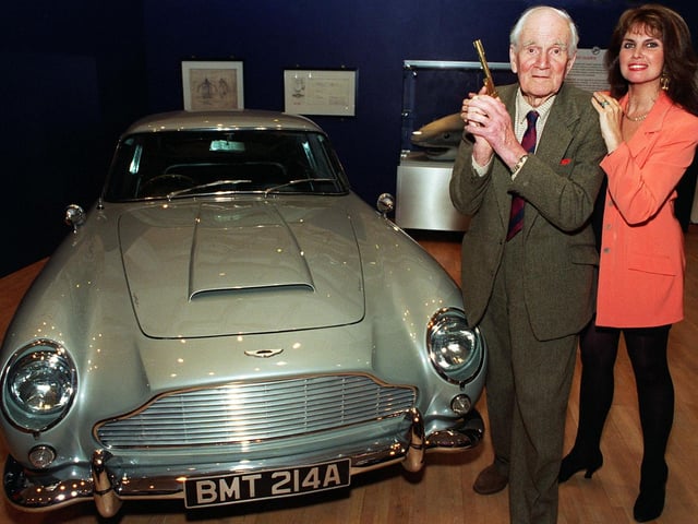 Desmond Llewelyn Q in the James Bond films  holding the original golden gun with Bond girl Caroline Munro alongside the Aston Martin one of the famous Bond cars at the 007 exhibition at the Royal Armouries in May 1997.