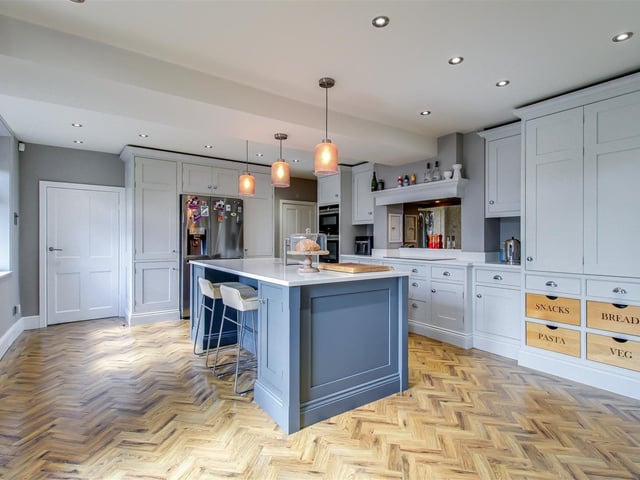 Features include a central island with a breakfast bar, a stainless steel sink, an integrated double oven and microwave, a dishwasher, and space for an American-style fridge freezer, as well as a five ring induction hob with an extractor hood.