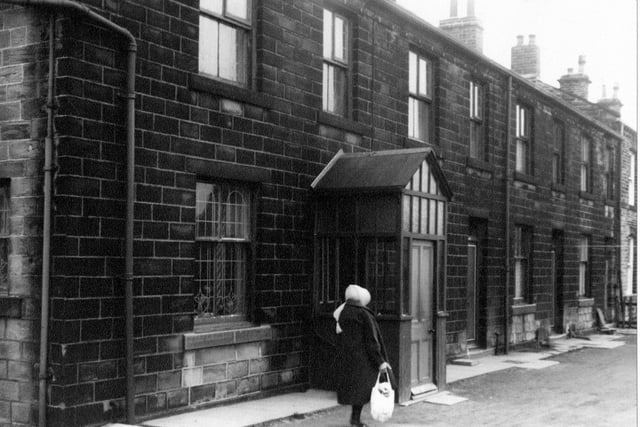 A woman in a headscarf and coat carries a bag up Whitehall Road in March 1967. The house on the left has been improved upon, unlike the others in the terrace, an enclosed porch of wood and glass has been added to the front door. The house displays patterned leaded glass windows.
