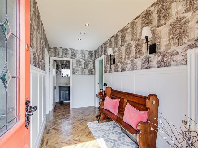 The entrance hall features a timber framed front door, decorative wall panelling, spotlights to the ceiling, and a central heating radiator.